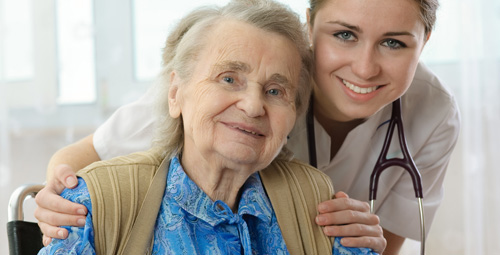 An older woman being hugged from behind by a healthcare professional